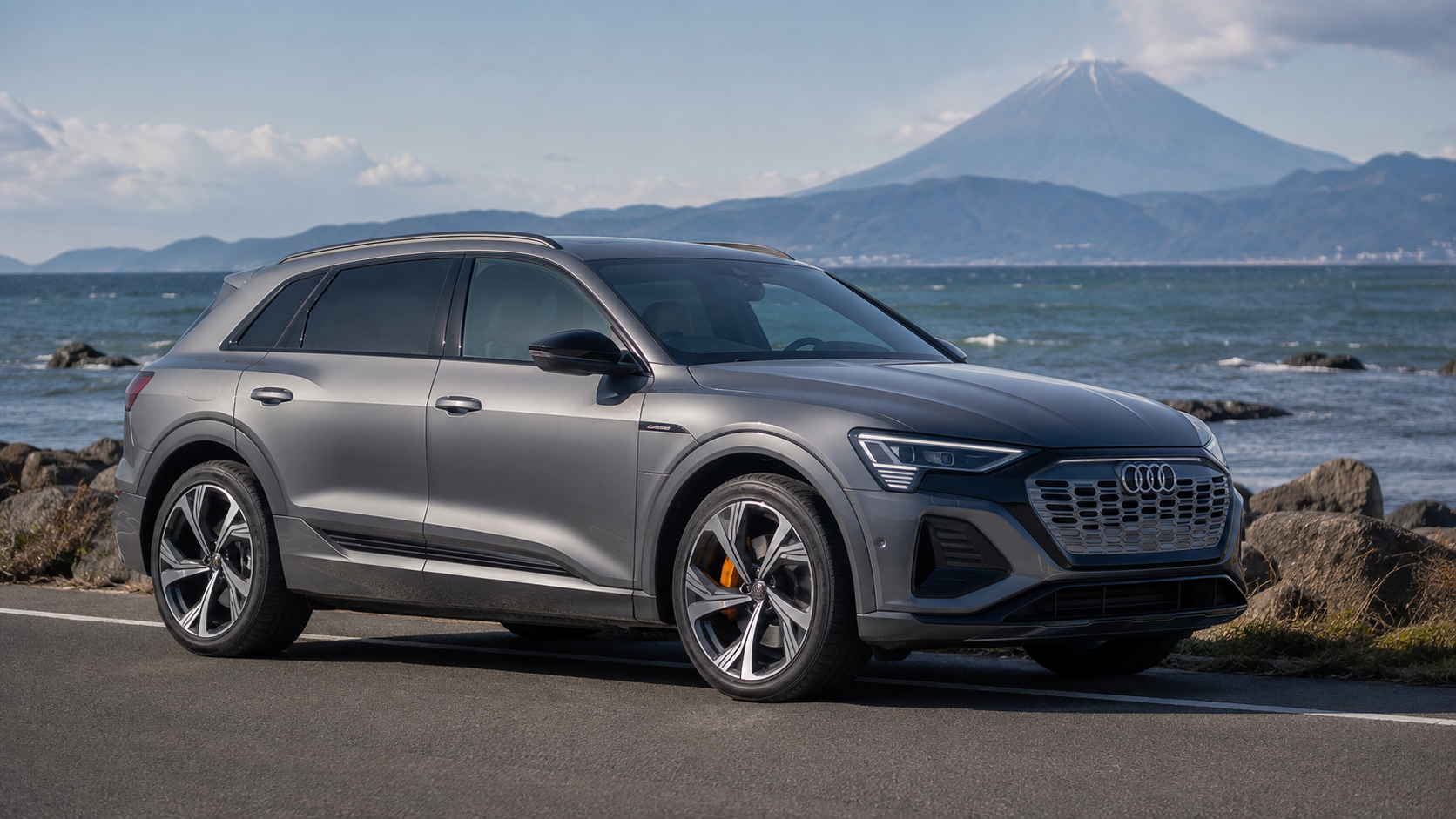 富士山と海岸をバックに立つグレーのアウディ Q8 e-tron EV SUVの外観